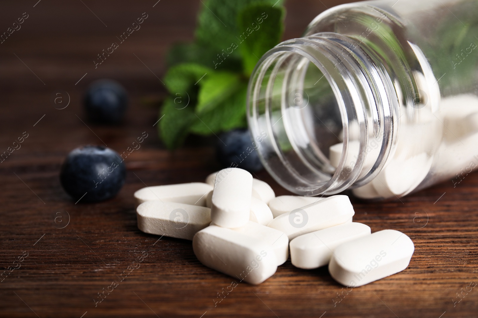 Photo of Bottle with vitamin pills and blueberries on wooden table, closeup
