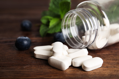 Photo of Bottle with vitamin pills and blueberries on wooden table, closeup