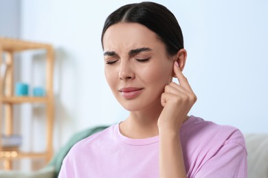 Young woman suffering from ear pain at home