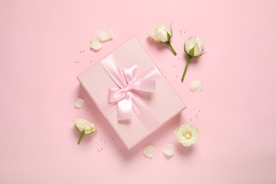 Photo of Elegant gift box and beautiful flowers on pink background, flat lay