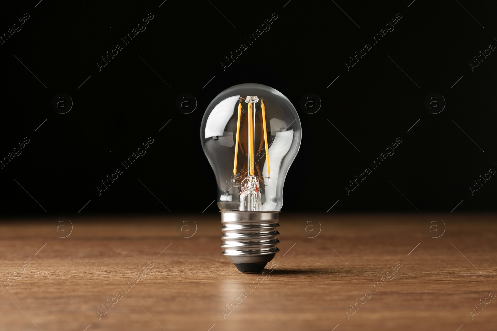 Photo of Vintage filament lamp bulb on wooden table against black background