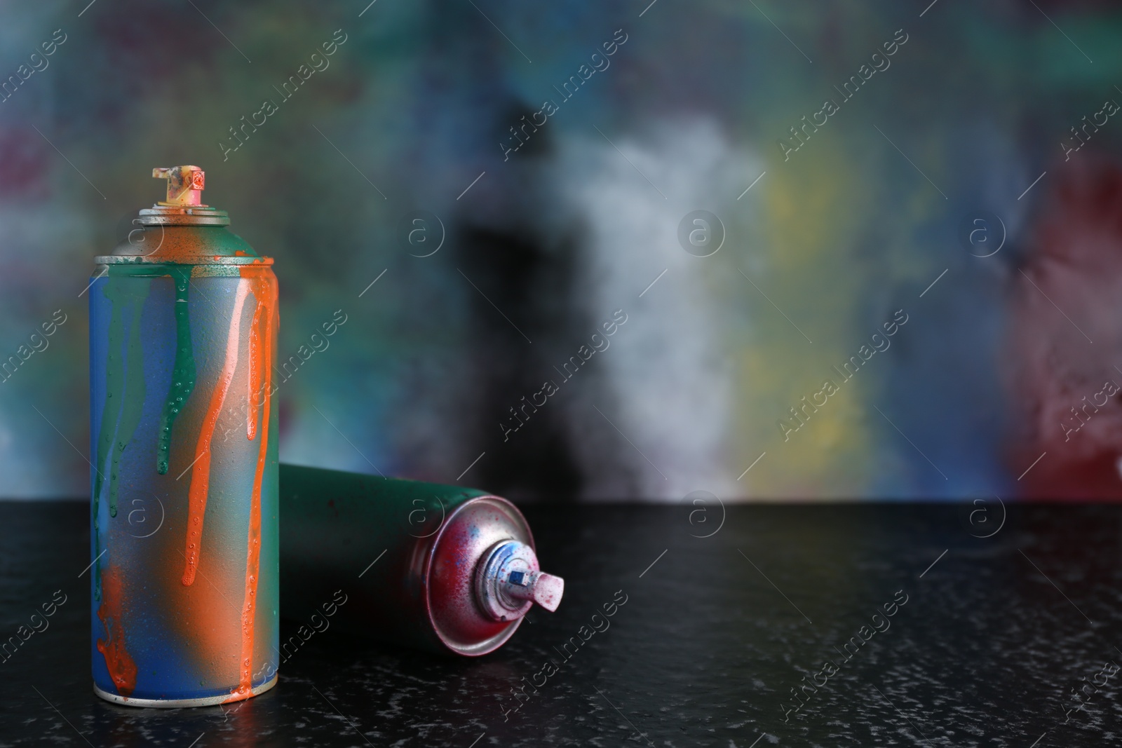 Photo of Two spray paint cans on black textured surface against color background, space for text