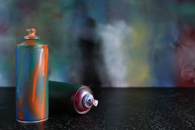 Photo of Two spray paint cans on black textured surface against color background, space for text