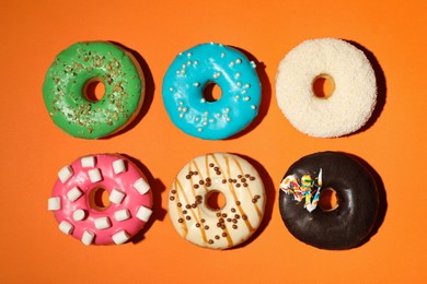 Photo of Different delicious glazed doughnuts on orange background, flat lay