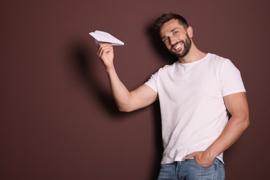Photo of Handsome man playing with paper plane on brown background. Space for text