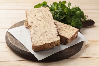 Photo of Pieces of tasty chocolate halva with mint on wooden table, closeup