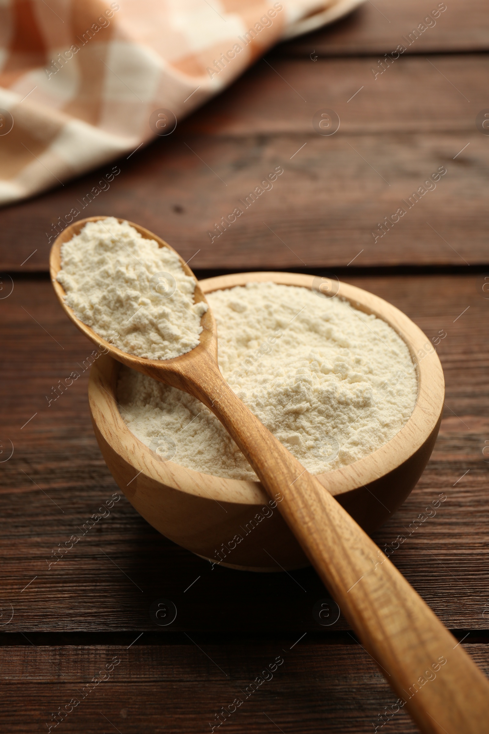 Photo of Baking powder in bowl and spoon on wooden table, closeup