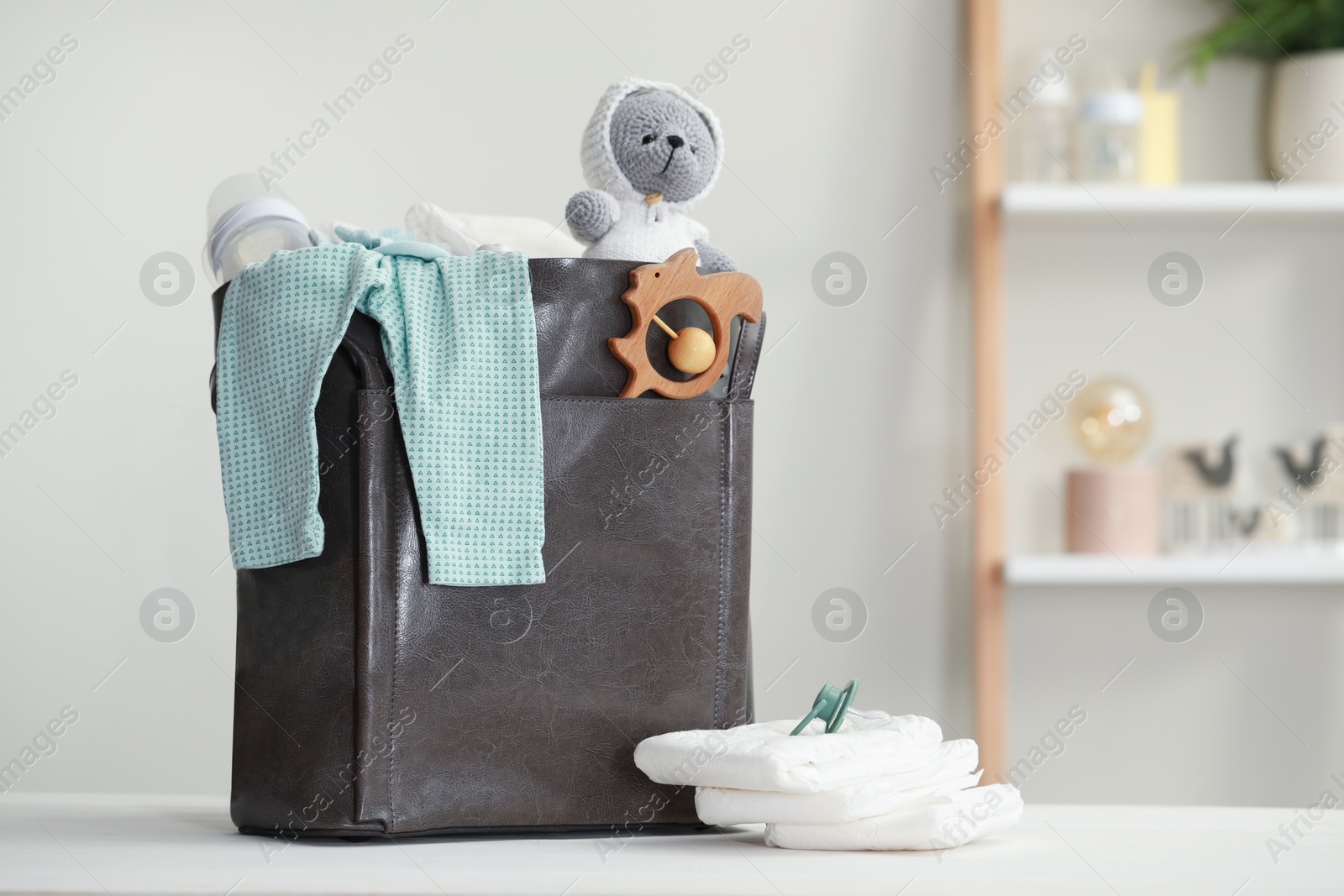 Photo of Mother's bag with baby's stuff on white wooden table indoors. Space for text