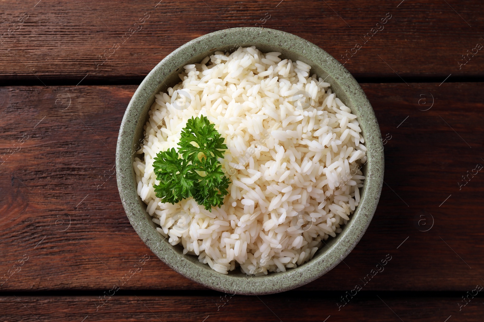 Photo of Delicious rice with parsley in bowl on wooden table, top view