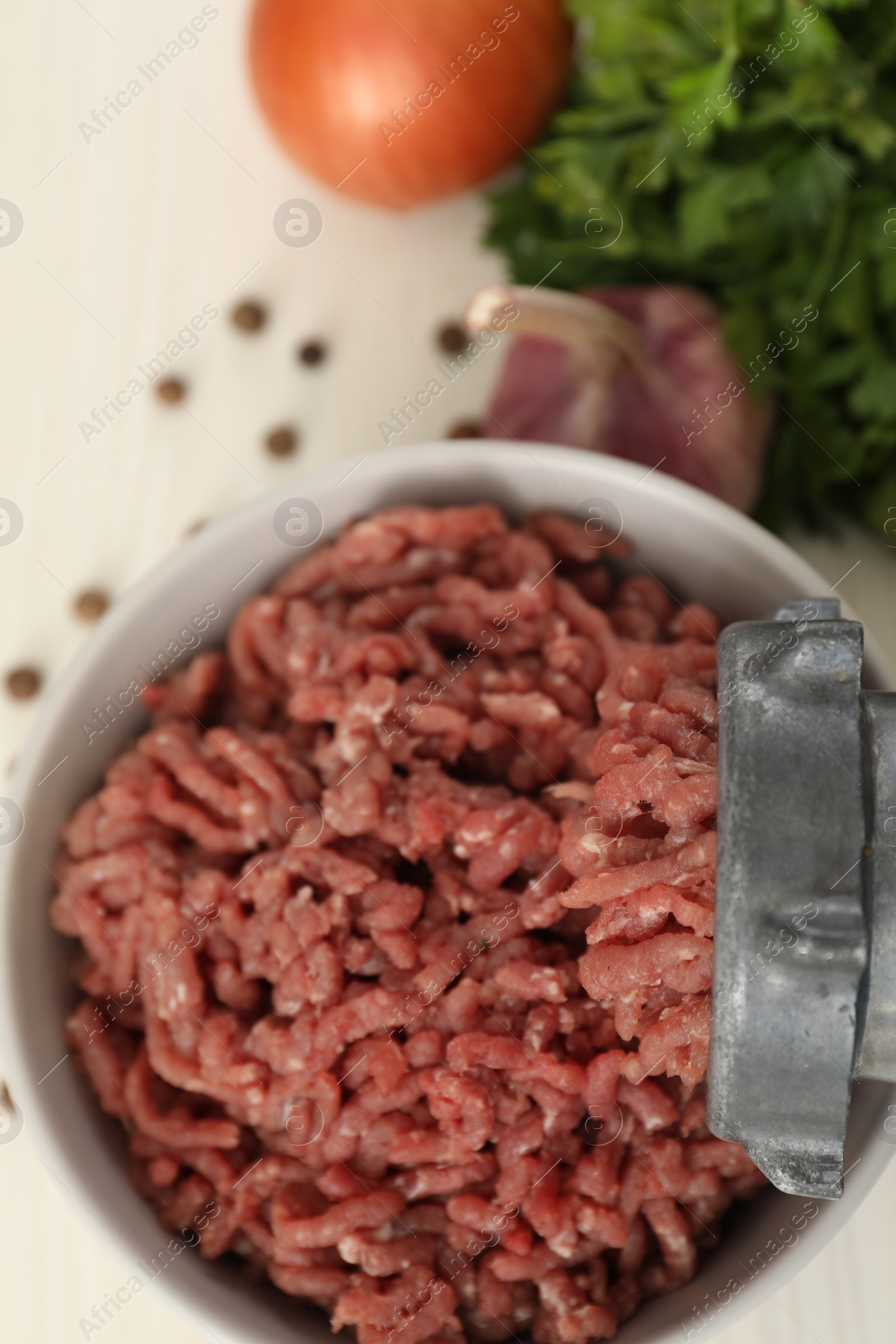 Photo of Mincing beef with meat grinder. Parsley, garlic and peppercorns on white table, flat lay