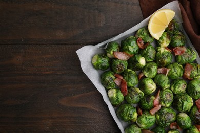Photo of Delicious roasted Brussels sprouts, bacon and lemon in baking dish on wooden table, top view. Space for text