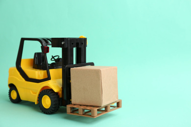 Photo of Forklift model and carton boxes on turquoise background, space for text. Courier service