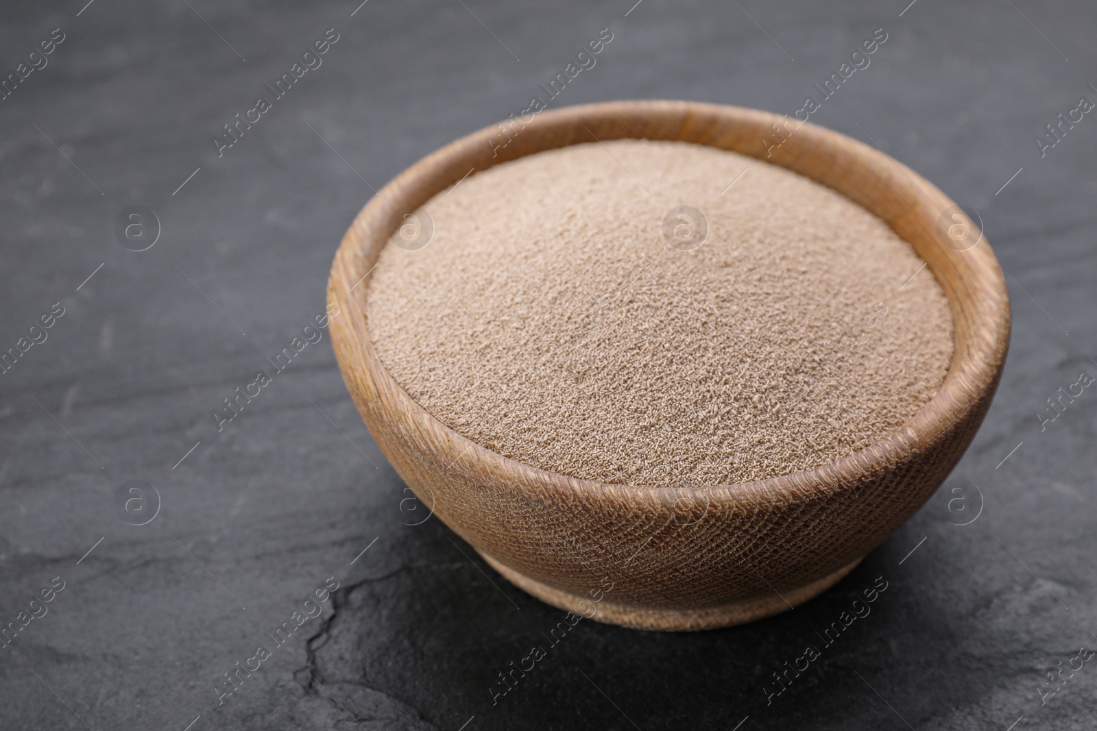 Photo of Bowl of active dry yeast on black table, closeup. Space for text