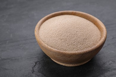 Bowl of active dry yeast on black table, closeup. Space for text