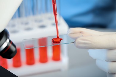 Scientist dripping sample of red liquid onto microscope slide in laboratory, closeup