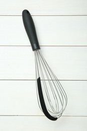 Metal whisk on white wooden table, top view