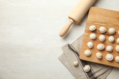 Photo of Board with raw dumplings and rolling pin on light background, flat lay. Space for text