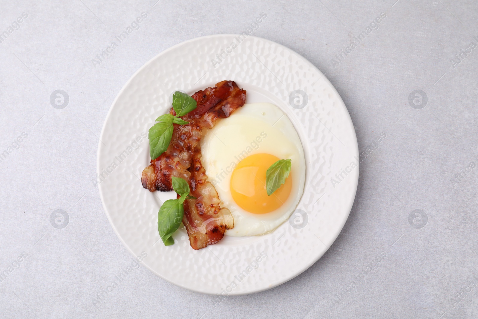 Photo of Fried egg, bacon and basil on light grey table, top view