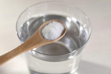 Photo of Spoon with baking soda over glass of water on light background, closeup