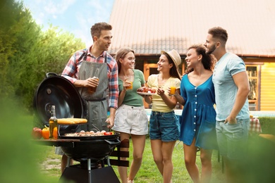 Photo of Group of friends with drinks near barbecue grill outdoors