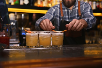 Photo of Bartender preparing tasty cocktail at table in nightclub, closeup