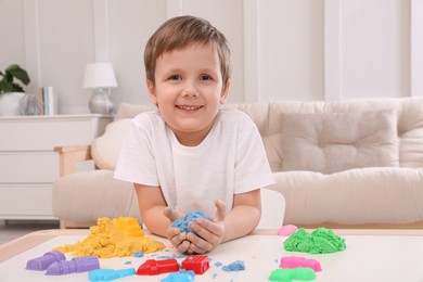 Photo of Cute little boy playing with bright kinetic sand at table in room