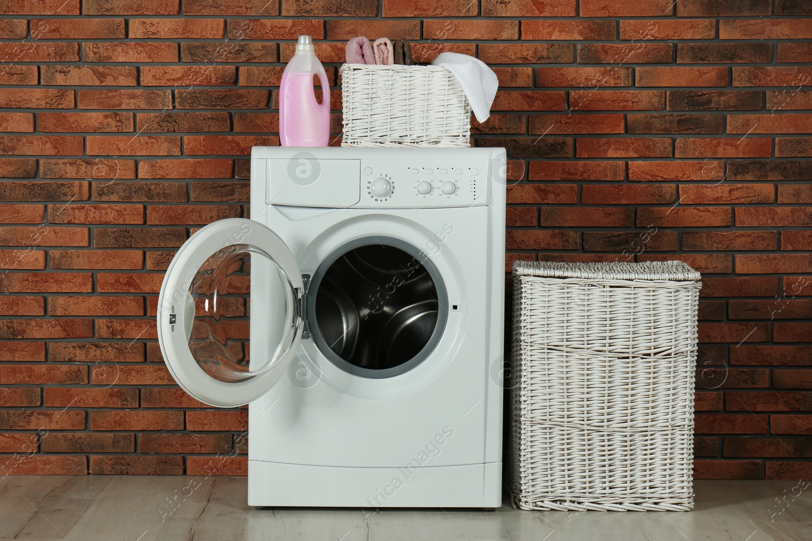 Photo of Modern washing machine with detergent and laundry baskets near brick wall
