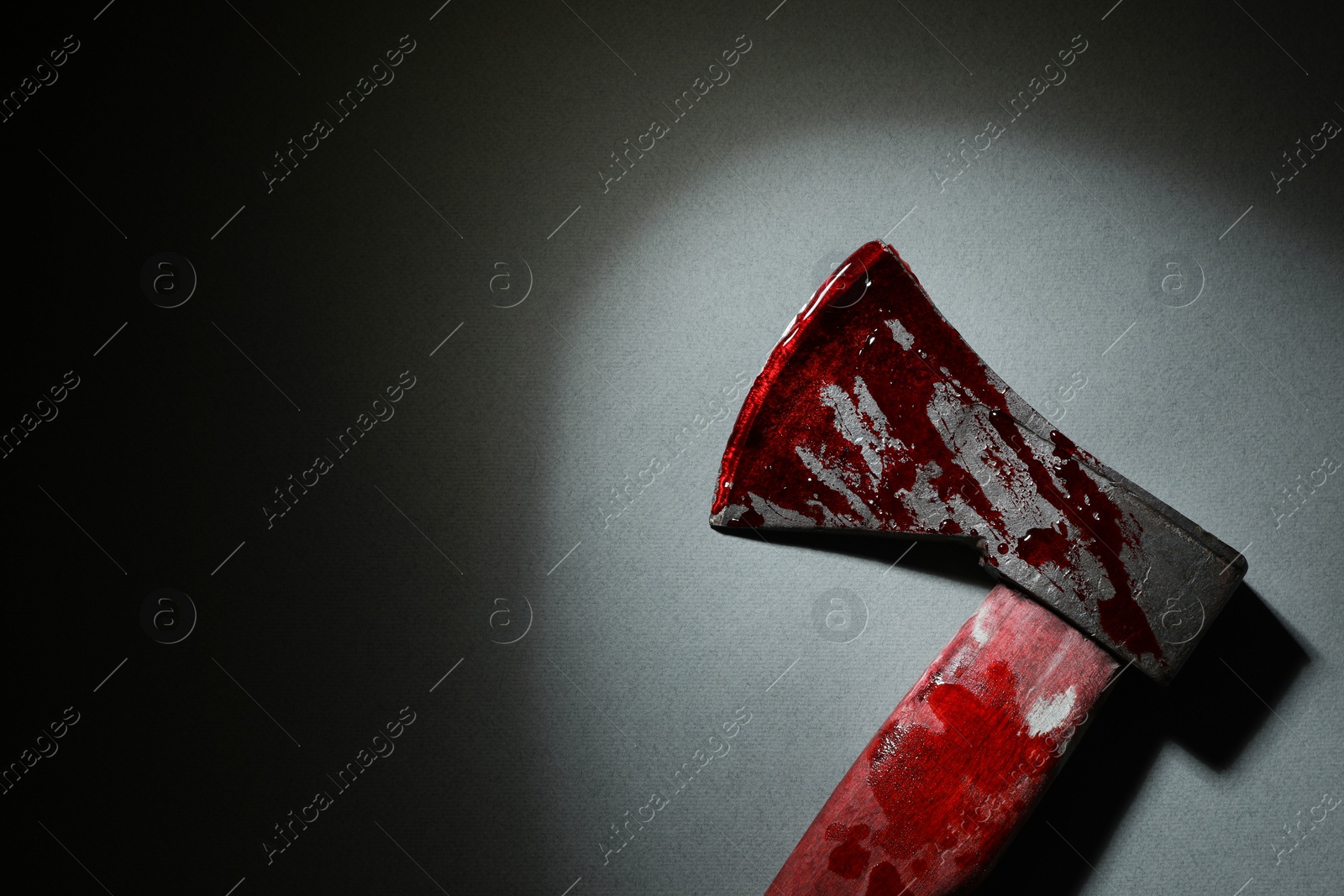 Photo of Axe with blood on gray surface in darkness, top view. Space for text