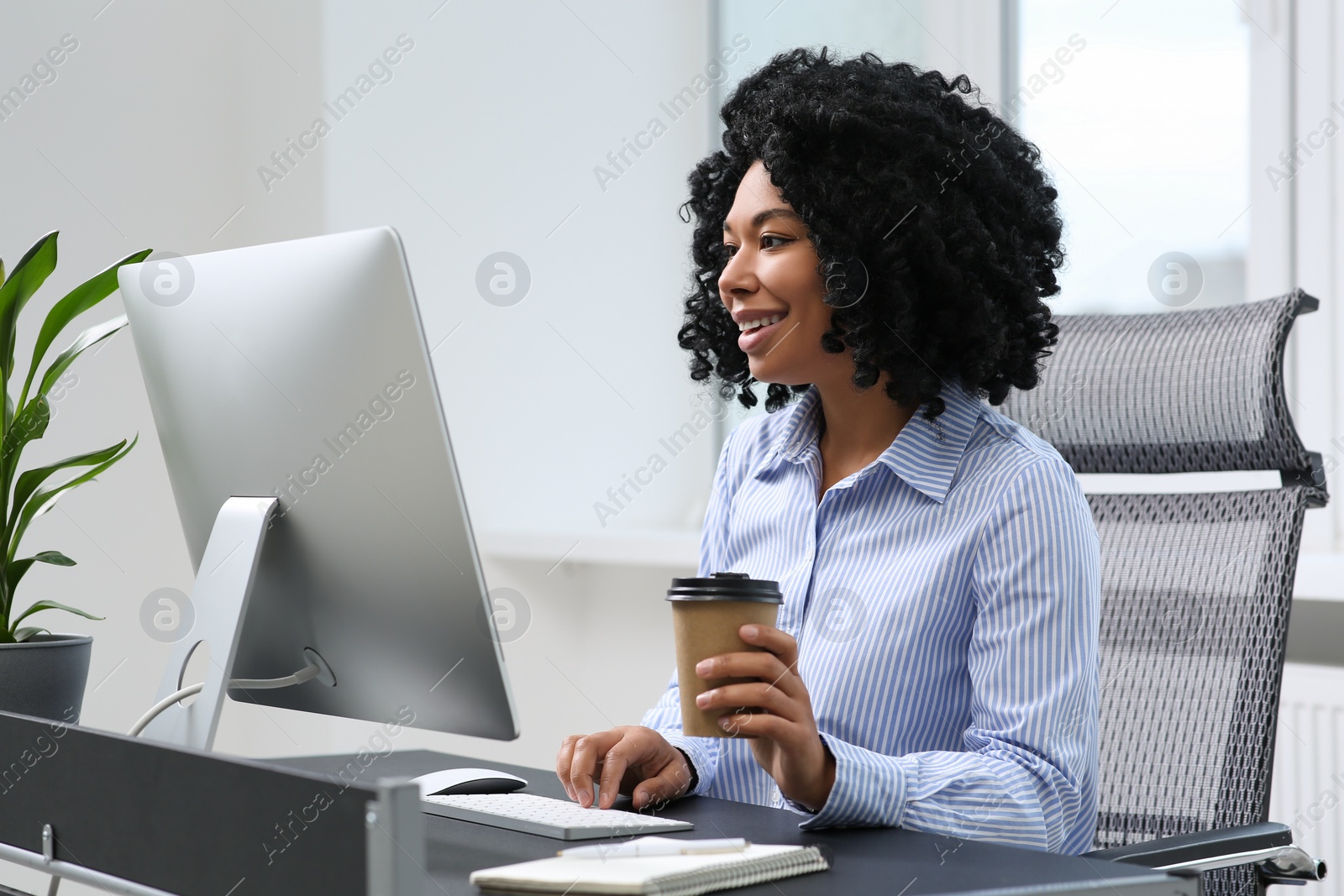 Photo of Young woman with cup of drink working on computer at table in office