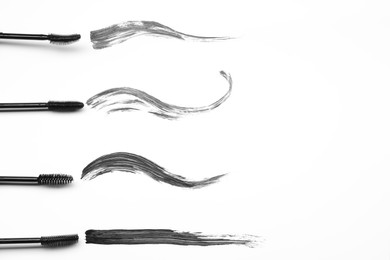 Photo of Smears of black mascara and applicators on white background, flat lay. Space for text