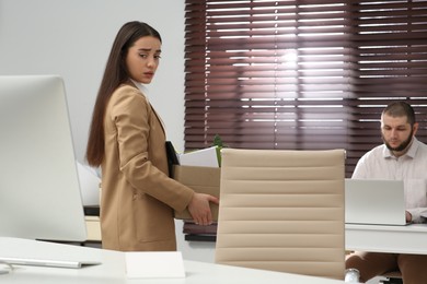 Photo of Upset dismissed woman carrying box with personal stuff in office