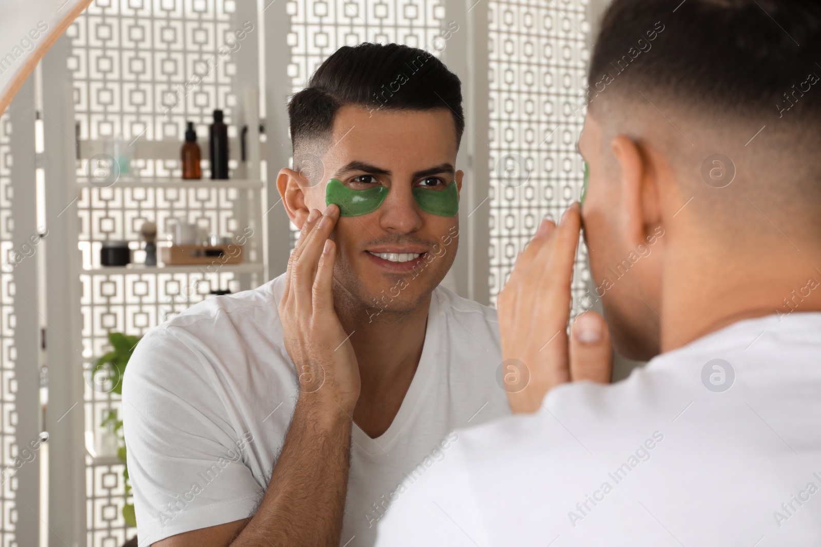 Photo of Man applying green under eye patch near mirror at home