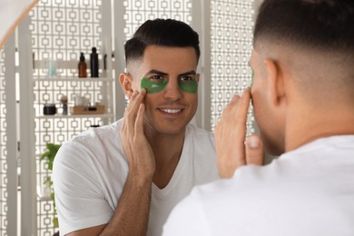 Man applying green under eye patch near mirror at home