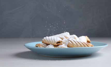 Photo of Woman with sieve sprinkling powdered sugar onto cookies at white wooden table, closeup