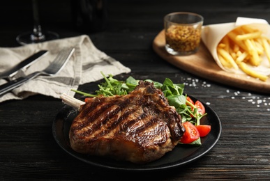Photo of Tasty grilled beef steak with salad on black wooden table