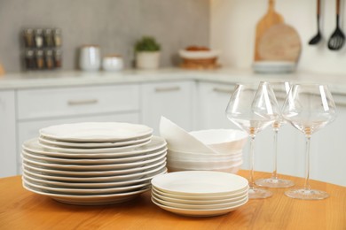 Clean plates, bowls and glasses on wooden table in kitchen