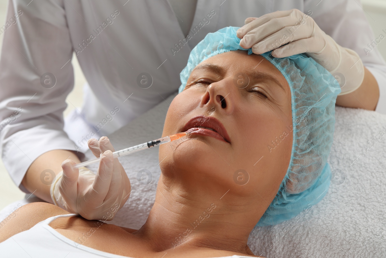 Photo of Doctor giving lips injection to senior woman in clinic, closeup. Cosmetic surgery