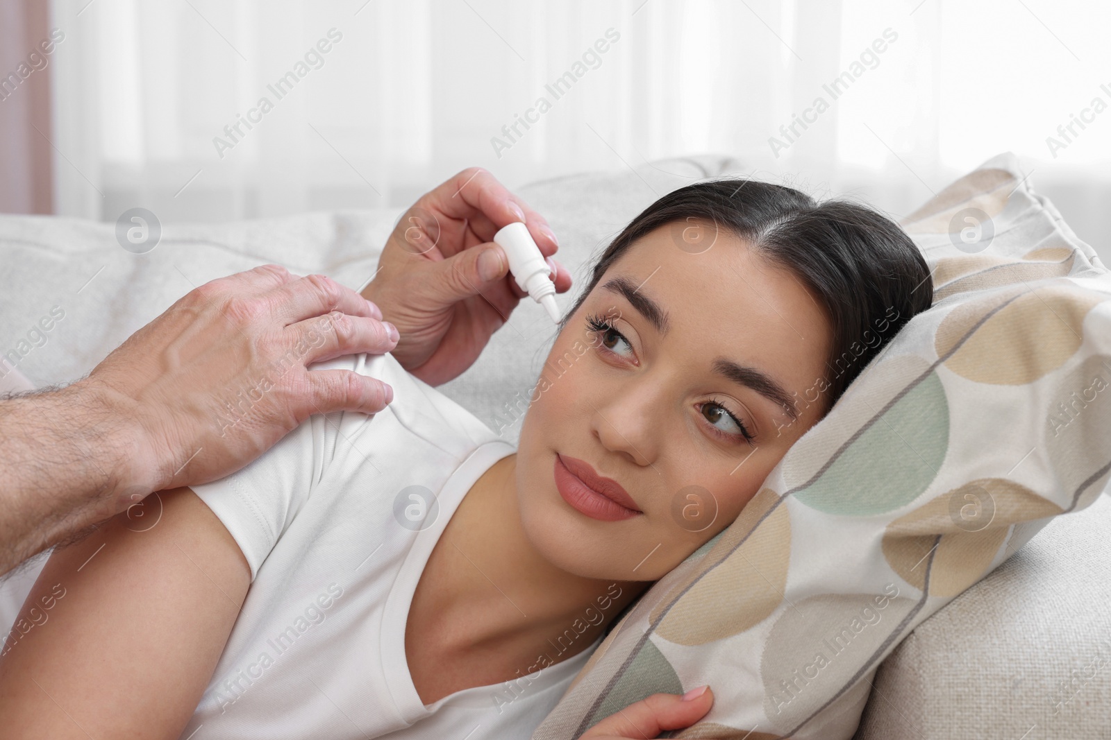 Photo of Senior man dripping medication into woman's ear on sofa at home