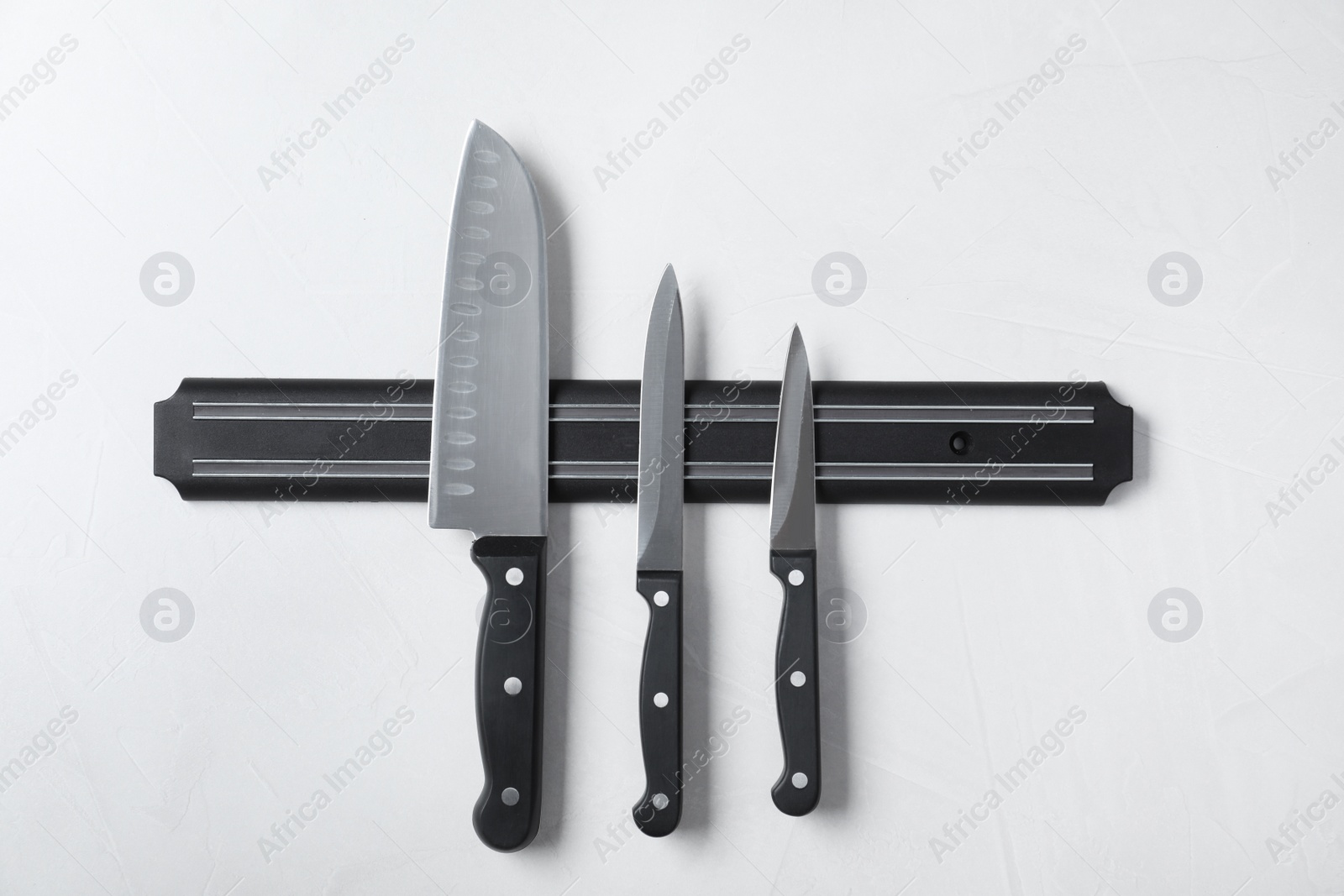 Photo of Magnetic holder with set of knives on grey stone background