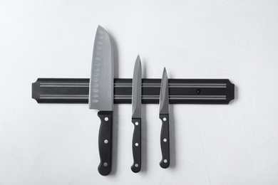 Photo of Magnetic holder with set of knives on grey stone background