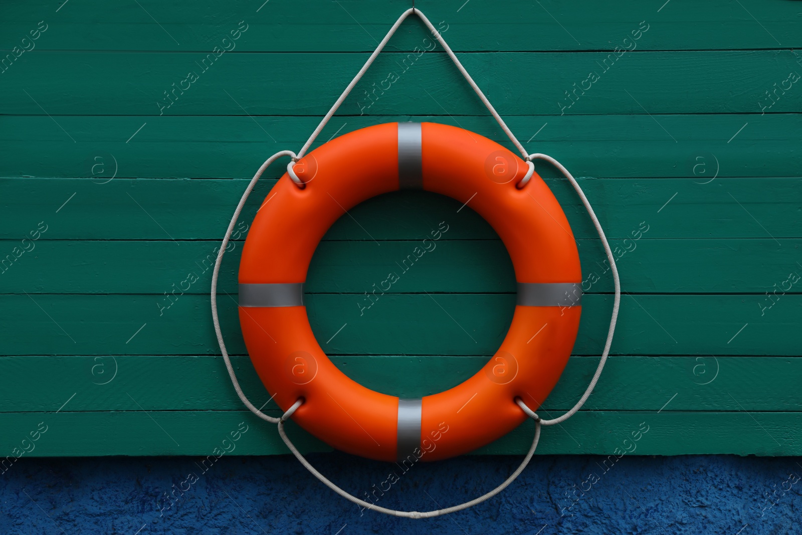 Photo of Orange lifebuoy hanging on green wooden board. Rescue equipment