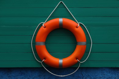 Photo of Orange lifebuoy hanging on green wooden board. Rescue equipment