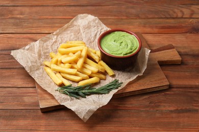Photo of Serving board with parchment, french fries, avocado dip and rosemary on wooden table