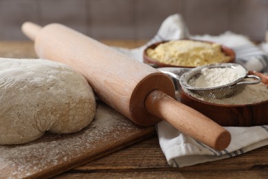 Rolling pin, flour and dough on wooden table, closeup