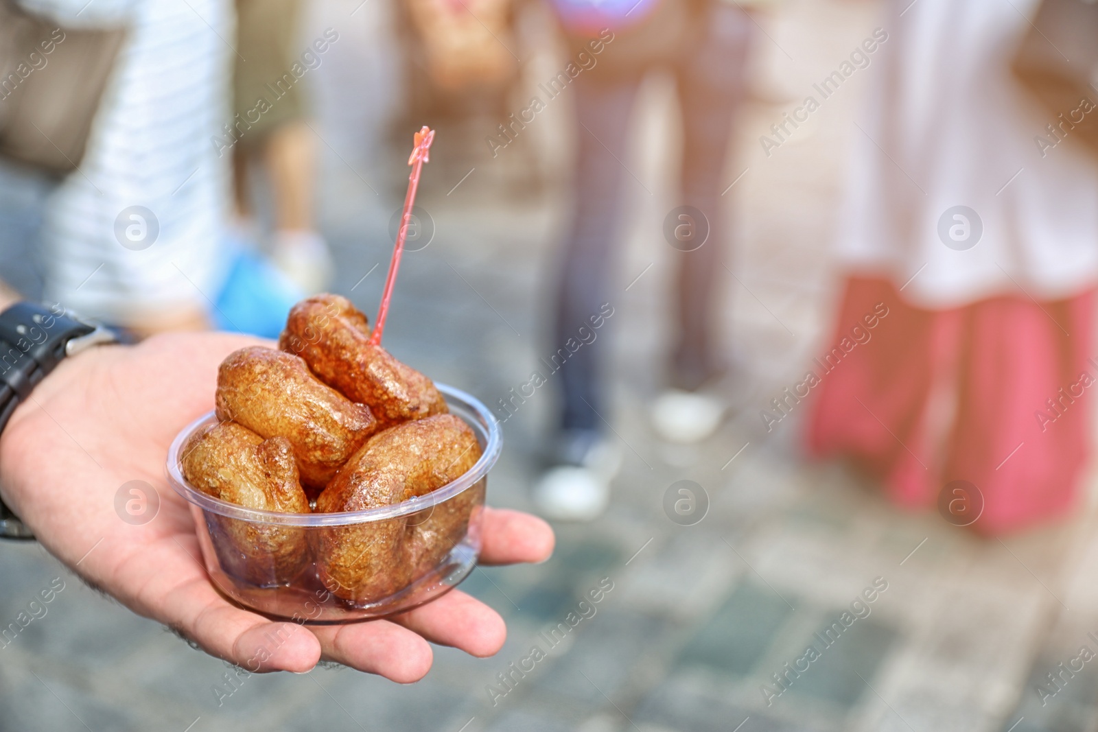 Photo of Man holding bowl with fresh lokma outdoors, closeup. Traditional Turkish treat