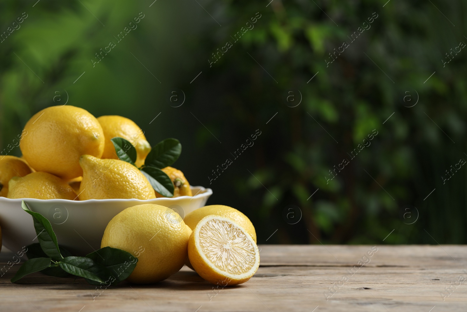 Photo of Fresh lemons and green leaves on wooden table. Space for text