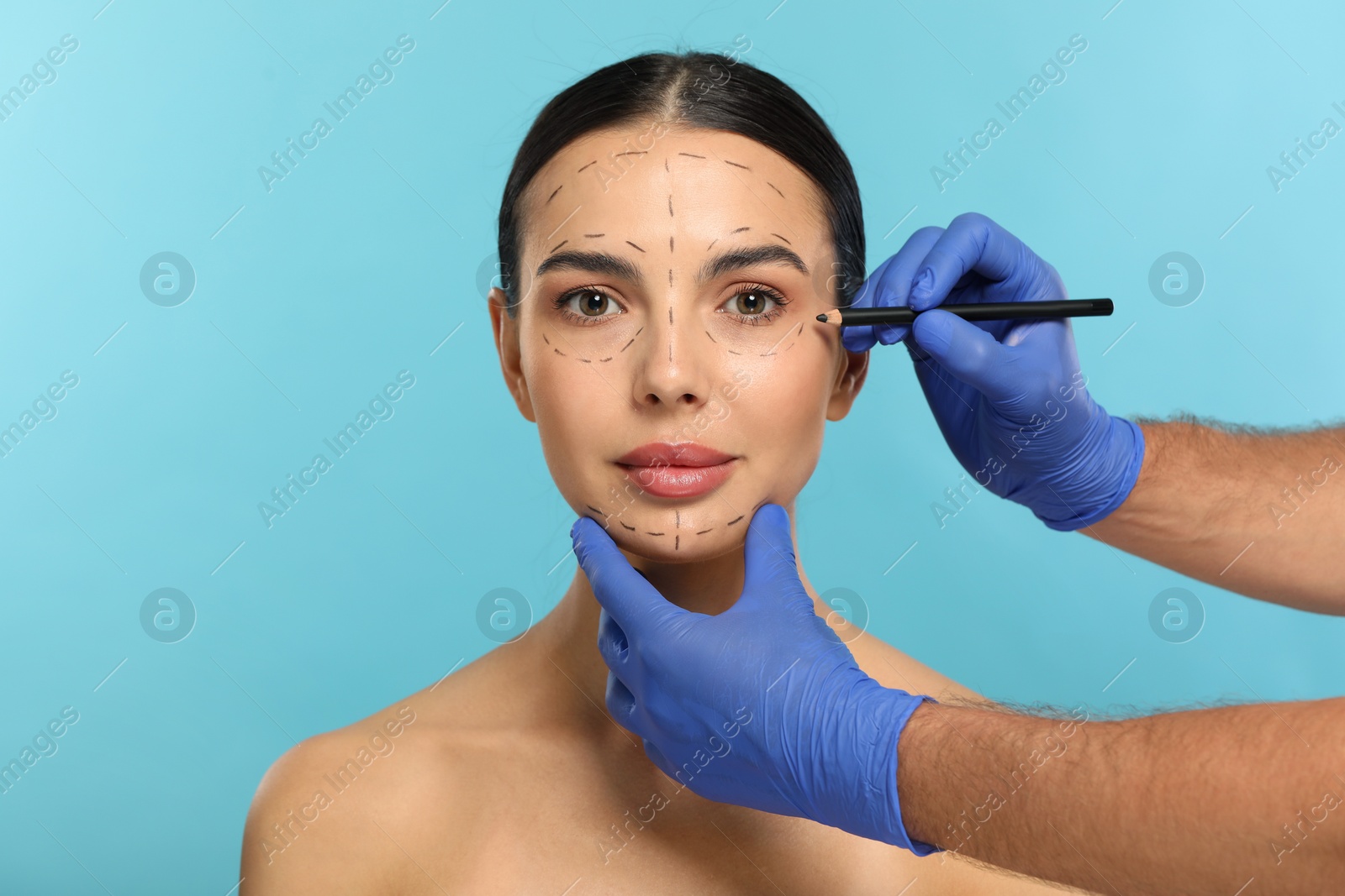 Photo of Doctor with pencil preparing patient for cosmetic surgery operation on light blue background