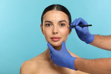 Doctor with pencil preparing patient for cosmetic surgery operation on light blue background