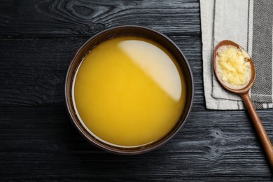 Photo of Bowl and spoon of Ghee butter on dark wooden table, flat lay