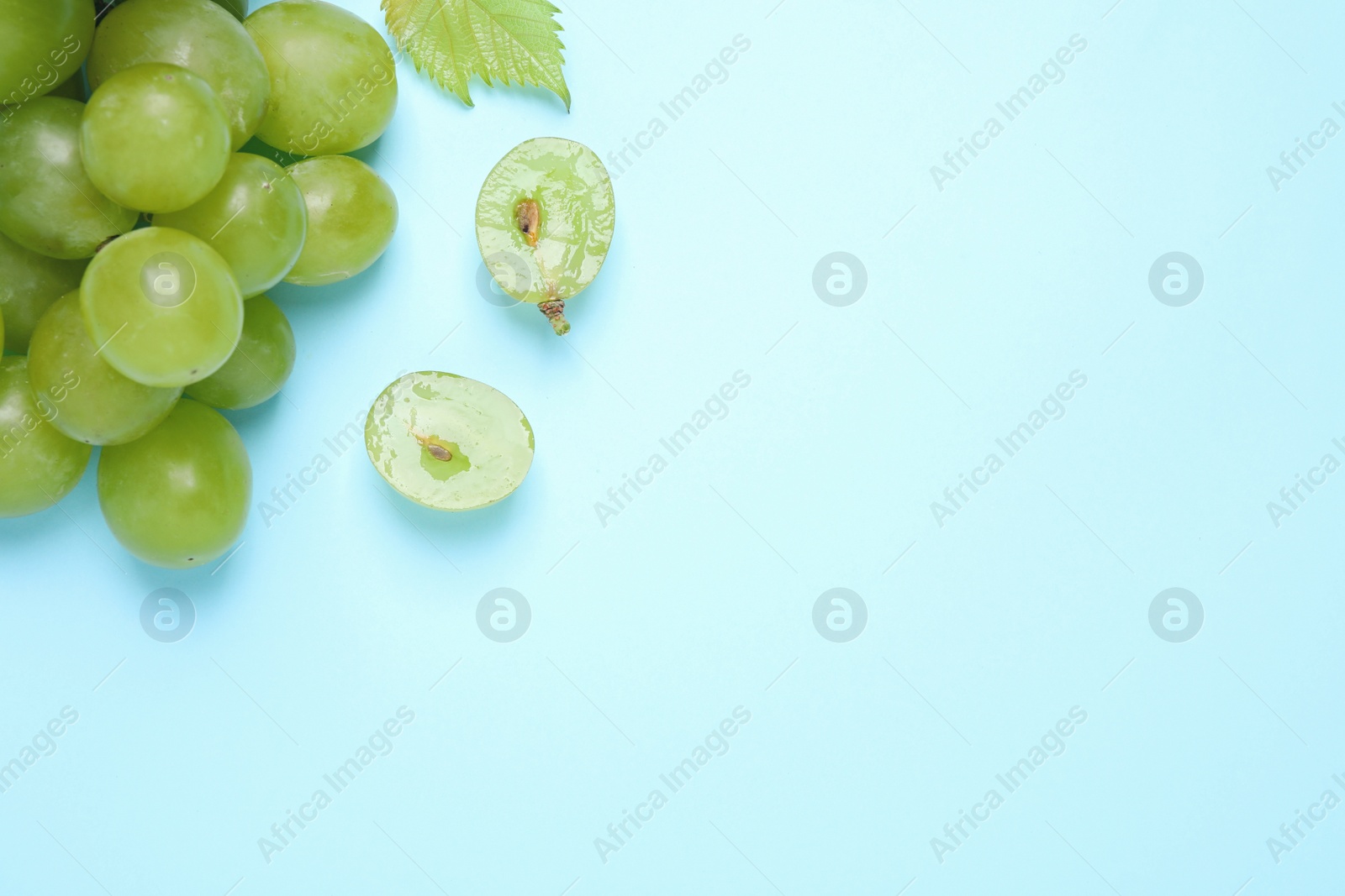 Photo of Ripe green grapes on light blue background, flat lay. Space for text